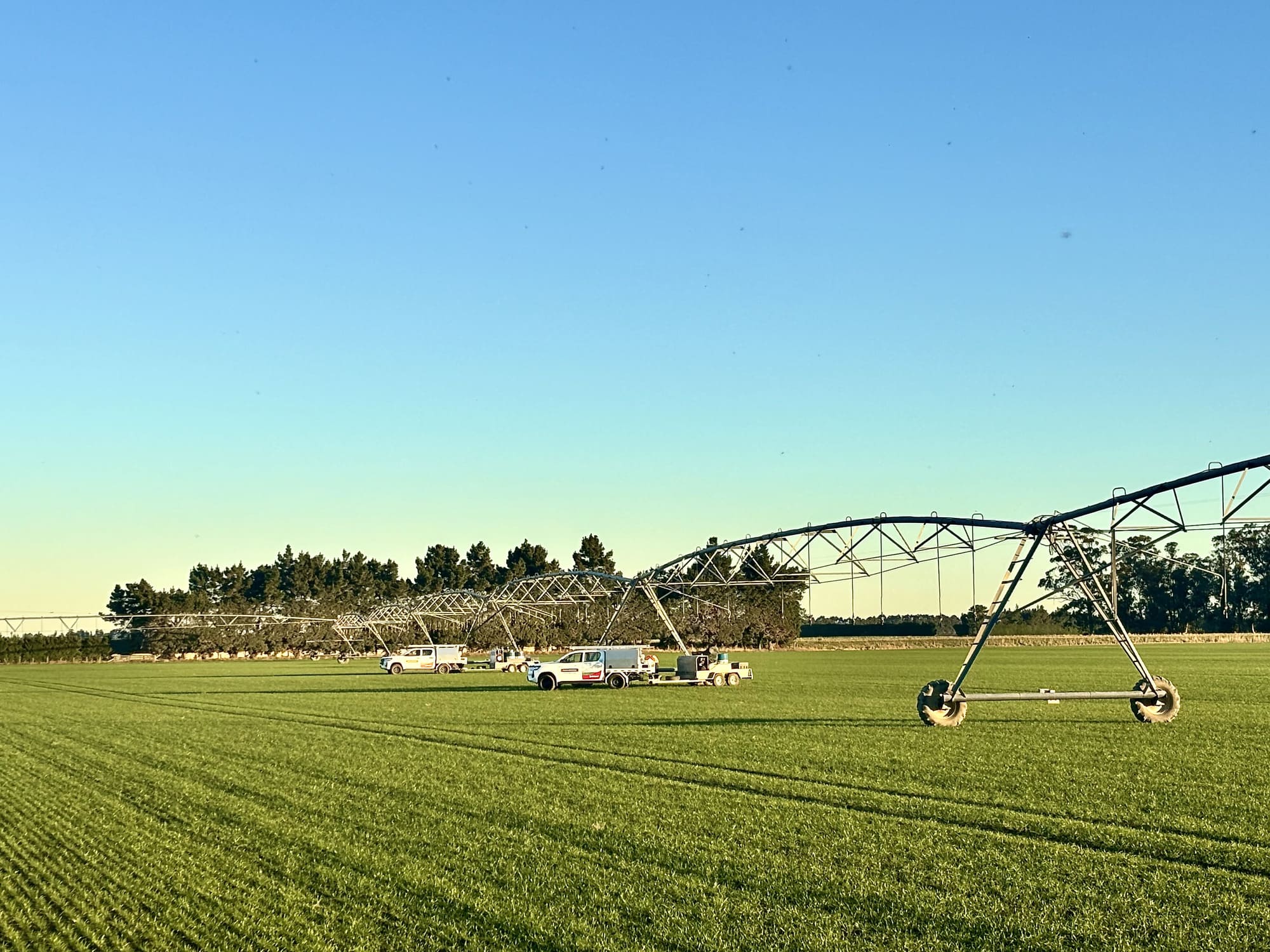 Center-pivot irrigation system in a green field with service trucks parked underneath.